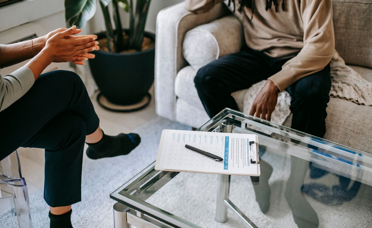 About Crop anonymous African American man in casual clothes sitting on sofa and talking to female psychologist during psychotherapy session in modern studio